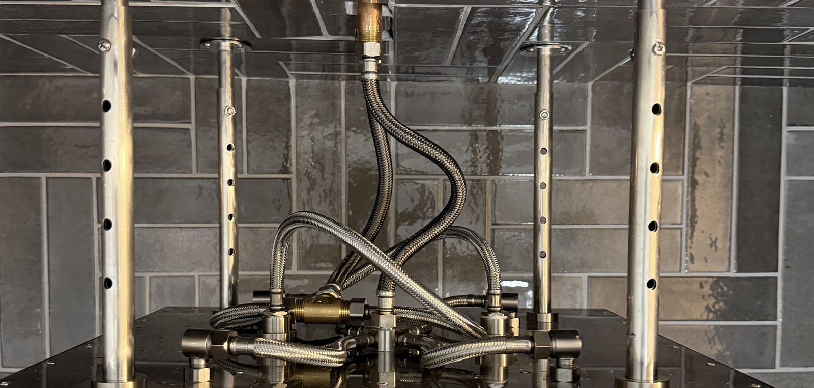 Overhead plumbing rough-in for the shower: brass fittings, valves and braided stainless supply lines feeding the rain panel and body sprays