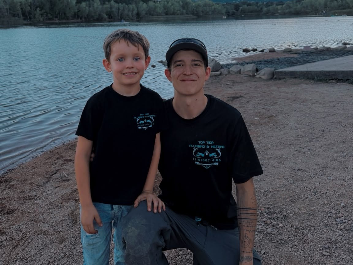 Tate of Top Tier Plumbing & Heating with his son at a Colorado Springs lake, both wearing the company shirt